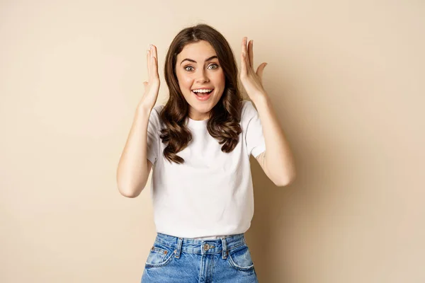 stock image Enthusiastic adn surprised woman winning, dancing and celebrating, standing in tshirt over beige background