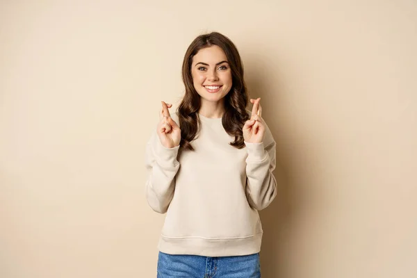 Confident woman praying, making wish with fingers crossed for good luck, standing over beige background — ストック写真