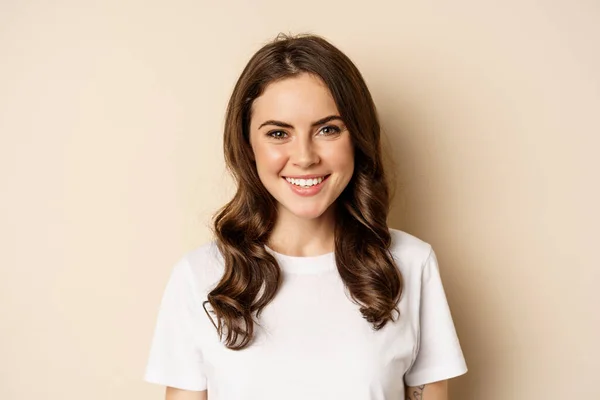 People. Close up portrait of young woman smiling, looking happy, wearing casual white t-shirt, standing healthy and cheerful against beige background — Fotografia de Stock