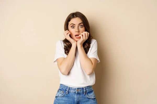Scared and shocked woman gasping, looking startled speechless, wearing t-shirt, standing over beige background — Stok fotoğraf