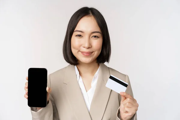 Mujer corporativa sonriente en traje, que muestra la pantalla del teléfono móvil y la aplicación en el teléfono móvil, la pantalla del teléfono inteligente, de pie sobre fondo blanco — Foto de Stock
