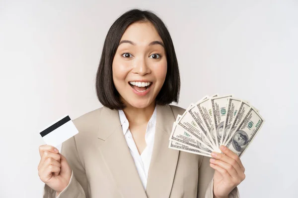 Entusiastiska unga asiatiska affärskvinna, visar pengar dollar och kreditkort, stående över vit bakgrund — Stockfoto