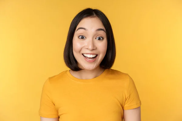 Nahaufnahme Porträt eines asiatischen Mädchens, das überrascht reagiert, erstaunt die Augenbrauen hebt, auf große Nachrichten reagiert, vor gelbem Hintergrund steht — Stockfoto