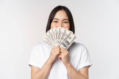 Dolarları tutan gülümseyen Asyalı kadının portresi, mikro kredi, finans ve nakit konsepti, beyaz arka planda duran