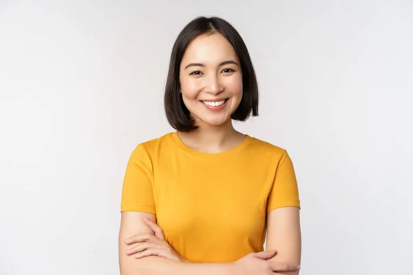 Genç, güzel esmer Asyalı kızın portresi gülümseyen ve mutlu görünen, kolları göğsünde, beyaz arka planda duran — Stok fotoğraf