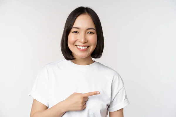 Mutlu Asyalı kız boş fotokopi alanında reklam gösteriyor, sağı gösteriyor ve gülümsüyor, afiş veya şirket logosu gösteriyor, beyaz arkaplan — Stok fotoğraf
