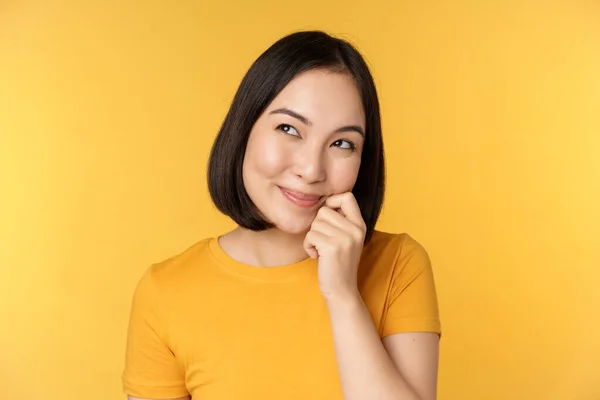 Yakışıklı Asyalı Kızın Gülümseyen Düşünen Düşünceli Sarı Arka Planda Tişörtle — Stok fotoğraf