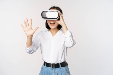 Vr sohbet. Asyalı kız sanal gerçeklik gözlükleriyle merhaba diyor, coşkuyla gülümsüyor, iletişim konsepti ve gelecek teknolojisi, beyaz arka plan.
