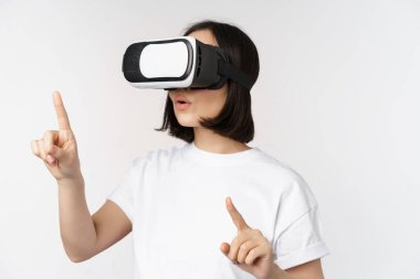 Sanal gerçeklik gözlüklü Asyalı kadın potansiyeli, beyaz arka planda duran, VR kulaklığı ile smth 'yi seçen,.