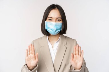 Coronavirus ve iş konsepti. Asyalı kadın ofis kadını portresi, iş yerinde tıbbi maske takan ve durduğunu gösteren bir kadın, içki yasağı hareketi, beyaz arka plan.