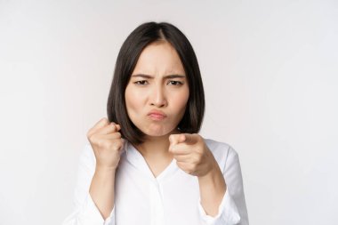 Kavgaya hazır, kavgaya hazır, beyaz arka planda duran kızgın genç kadın yumruklarını yaklaştır..