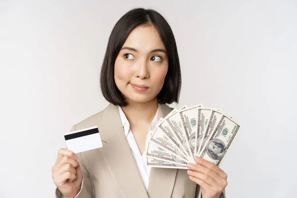 韓国の企業の女性がクレジットカードと現金を提示し 手にドルを持ち 白い背景の上に立って考え — ストック写真