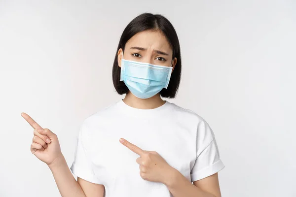 Sorgsen Asiatisk Kvinna Medicinsk Mask Pekar Finger Vänster Rynkar Pannan — Stockfoto