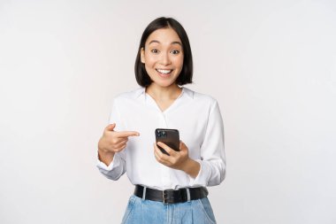 Akıllı telefon uygulaması hakkında konuşan, kameraya bakarken telefonu işaret eden, beyaz arka planda duran harika bir kız..