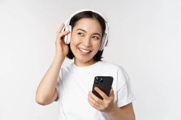 Hermosa Chica Asiática Moderna Escuchando Música Auriculares Sosteniendo Teléfono Móvil —  Fotos de Stock