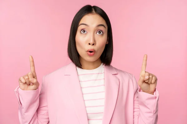 Entusiasta trabajadora corporativa, mujer de negocios asiática señalando con los dedos hacia arriba y sonriendo, mostrando publicidad, logotipo, de pie sobre fondo rosa —  Fotos de Stock