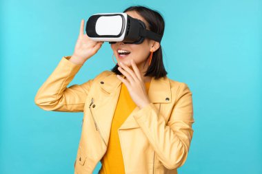VR kulaklık takan mutlu Asyalı kadın modelin portresi. Sanal gerçeklik gözlükleriyle gülüyor ve gülümsüyor. Mavi arka planda duruyor.