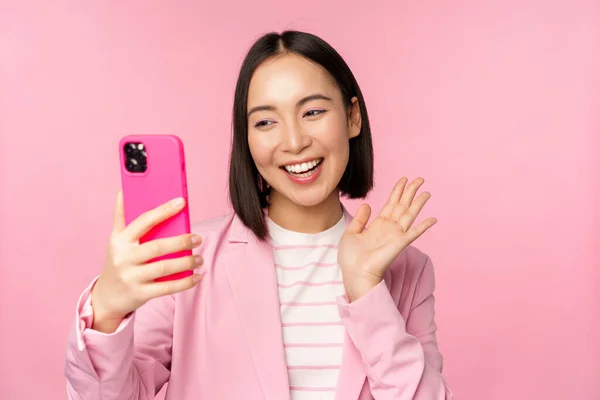 Elegante donna d'affari asiatica, ragazza in giacca e cravatta scattare selfie su smartphone, video chat con app per cellulare, posa sullo sfondo rosa dello studio — Foto Stock