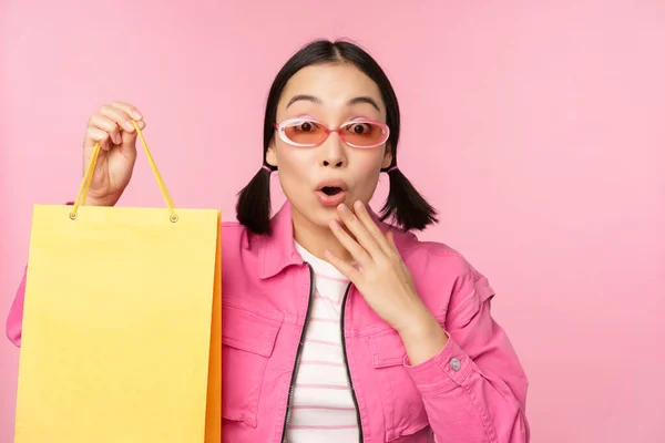 쇼핑. 선글라스 를 쓴 세련 된 동양 소녀, 가게에서 가방을 들고 미소를 짓는 모습, 상점에서 판매 프로 모 를 추천하는 핑크 색 배경 위에 서 있는 모습 — 스톡 사진