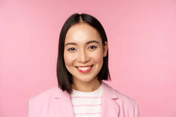 전문적으로 보이고, 카메라 앞에서 웃고, 양복을 입고, 핑크 색 배경 위에 서 있는 이시아 회사 여성의 사진을 클로즈업합니다. — 스톡 사진
