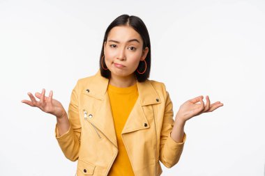 Kafası karışmış genç Asyalı kadının omuzlarını silkmesi, kameraya şaşkın ve bilgisiz bakması, anlayamaması, beyaz arka planda durması.