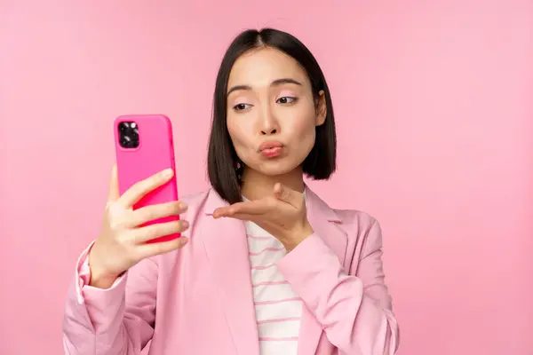 Snygg asiatisk affärskvinna, flicka i kostym tar selfie på smartphone, videochatt med mobiltelefon app, poserar mot rosa studio bakgrund — Stockfoto