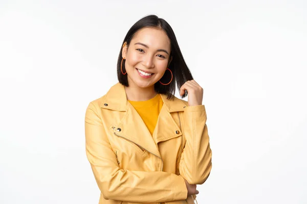Retrato de mulher asiática em casaco amarelo, sorrindo e olhando feliz, de pé sobre fundo branco — Fotografia de Stock