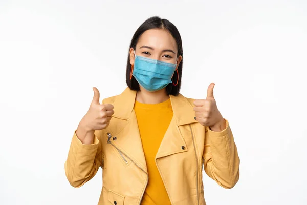 親指を示す医療面マスクの笑顔アジアの女性, covid-19から保護具を身に着けているサポート,コロナウイルスパンデミック,白の背景 — ストック写真