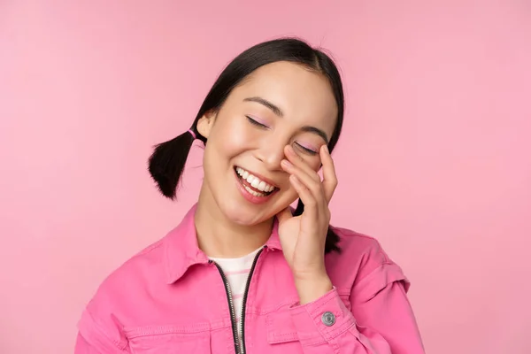 열정적 이고 웃고 웃으며 분홍색 배경에 반해서 행복하게 서 있는 아름다운 아시아인 소녀의 사진을 클로즈업하 세요. — 스톡 사진