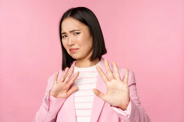 Aléjate. Asqueada mujer de negocios asiática rechazando, estrechando la mano para rechazar, haciendo muecas de aversión, declinando smth con aversión, posando en traje sobre fondo rosa —  Fotos de Stock