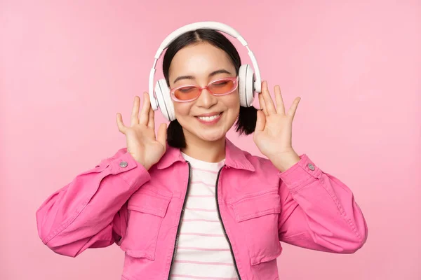 Bailando elegante chica asiática escuchando música en auriculares, posando sobre fondo rosa — Foto de Stock