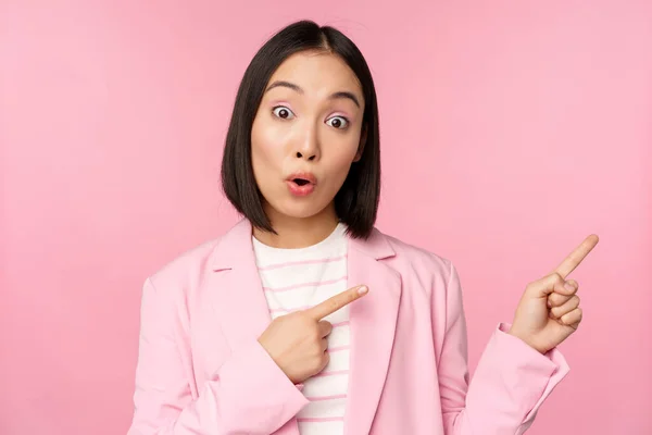 Entuzjastyczna profesjonalna bizneswoman, sprzedawczyni wskazująca palcem w prawo, pokazując reklamę lub logo firmy na bok, pozowanie na różowym tle — Zdjęcie stockowe