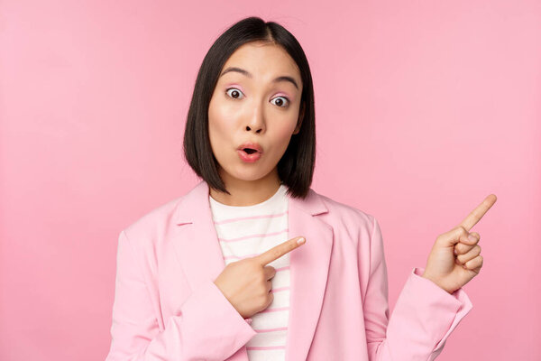 Enthusiastic professional businesswoman, saleswoman pointing fingers right, showing advertisement or company logo aside, posing over pink background