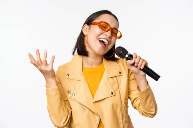 Mikrofon tutan, karaokede şarkı söyleyen, beyaz arka planda duran bir kız.