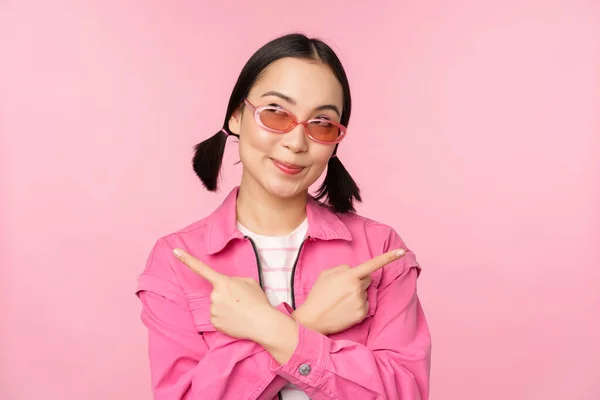 선택. 우아 한 금발 소녀, 아시아 여성 모델은 손가락을 옆으로 가리키며 분홍색 배경 위에 서 있는 두 가지 변형 제품 광고를 보여 주고 있다. — 스톡 사진