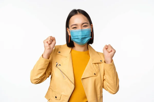 Covid-19 e conceito de pessoas. Jovem mulher asiática em máscara facial médica, dançando feliz em roupas casuais, posando sobre fundo branco — Fotografia de Stock