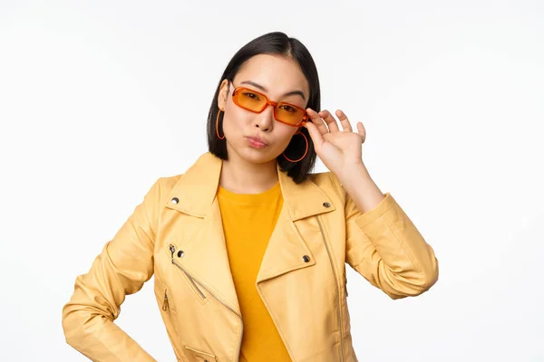 Elegante modelo femenino asiático, lleva gafas de sol, se ve seguro y fresco, se levanta sobre fondo blanco — Foto de Stock