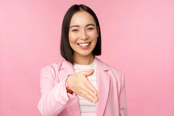 Портрет усміхненої, приємної бізнес-леді, що тремтить руками бізнес-партнера, рукостискання, розтягування руки і привітання, стоячи над рожевим тлом — стокове фото