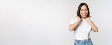 Yakışıklı, güzel Asyalı kadının portresi yeni saç kesimine dokunuyor, saç stilini gösteriyor, kameraya gülümsüyor, beyaz arka planda duruyor.