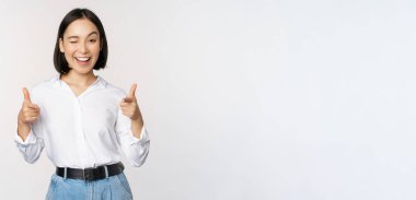 Tebrik ederim. Gülümseyen çekici Asyalı kadın, iş kadını mutlu bir yüzle kamerayı işaret ediyor, iltifat ediyor, davet ediyor, beyaz arka planda duruyor.