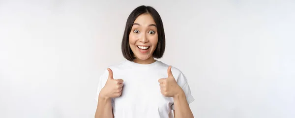 Happy young korean woman showing thumbs up and smiling, give positive feedback, recommending smth, standing over white background — Stock Photo, Image