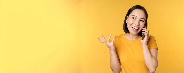 Jovencita coreana hablando por teléfono móvil. Mujer asiática llamando en el teléfono inteligente, de pie sobre fondo amarillo — Foto de Stock