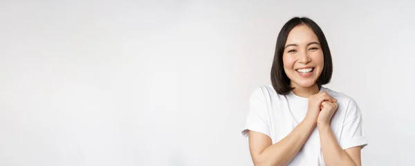 Retrato de una hermosa mujer coreana con una sonrisa blanca saludable, riendo y mirando feliz a la cámara, de pie en camiseta sobre fondo blanco del estudio — Foto de Stock