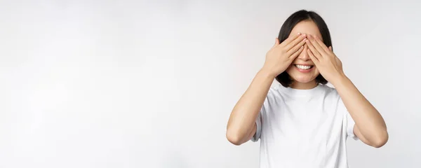 Retrato de mujer asiática cubriendo ojos, esperando sorpresa con los ojos vendados, sonriendo feliz, anticipando, de pie sobre fondo blanco —  Fotos de Stock