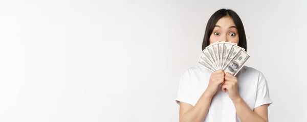 Happy asian girl holding money, cash near face, concept of microcredit and finance, white studio background — Stock Photo, Image