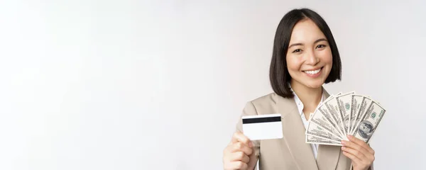 Zbliżenie Azji businesswoman, biuro pani pokazując karty kredytowe i pieniądze dolarów, stojąc w garniturze na białym tle — Zdjęcie stockowe
