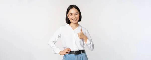 하얀 배경 위에 서 있는, 마치 좋은 것처럼 추천하면서, 엄지손가락을 들고 승인하고 있는 자신감 있는 아시아 여인의 이미지 — 스톡 사진
