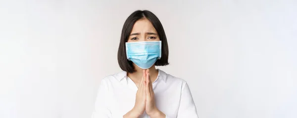 Portrait de femme asiatique dans le masque facial médical de covid, suppliant, demandant de l'aide, dire s'il vous plaît, debout sur fond blanc — Photo