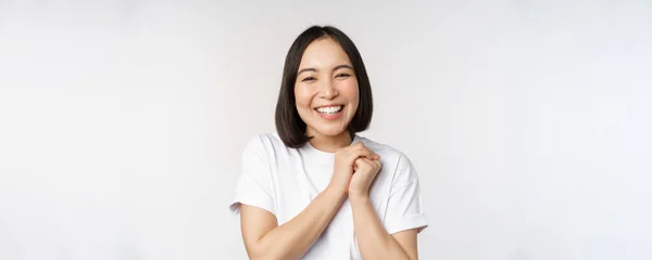 Retrato de una hermosa mujer coreana con una sonrisa blanca saludable, riendo y mirando feliz a la cámara, de pie en camiseta sobre fondo blanco del estudio —  Fotos de Stock