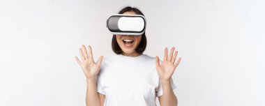 Mutlu Asyalı kadın VR kulaklık kullanıyor, el sallıyor ve gülüyor, sanal gerçeklik gözlüğü kullanıyor, beyaz arka planda duruyor.
